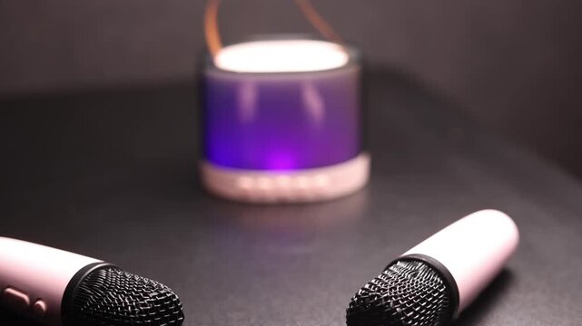 Two pink portable karaoke microphones and a colorful Bluetooth speaker on a dark surface