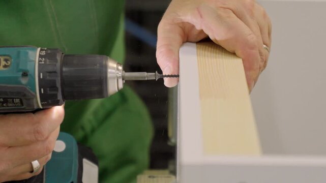 Close-up of a factory worker using a screwdriver to assemble cabinet furniture from MDF slabs, highlighting the industrial production process and craftsmanship.