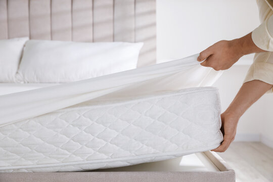 Man putting bed sheet on mattress indoors, closeup