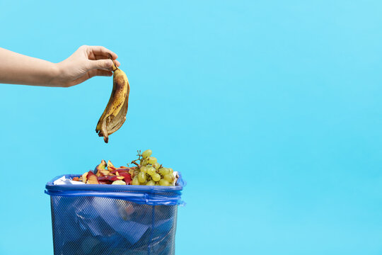 Woman throwing banana peel into garbage can on light blue background, closeup. Space for text