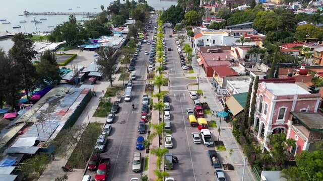 Drone footage advancing along Ramon Corona Avenue, Chapala, Mexico. Busy street with cars, buildings, palm trees, and Lake Chapala shoreline visible