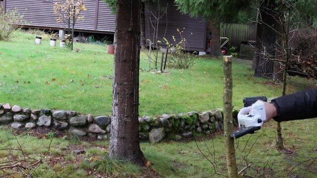 Man trims tree branches with cordless chain saw for pruning trees, right view. High quality 4k footage