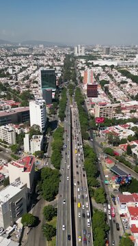 High angle drone view of Lazaro Cardenas Avenue, a major urban road with heavy traffic flow in a modern city, flanked by buildings and trees under a clear sky