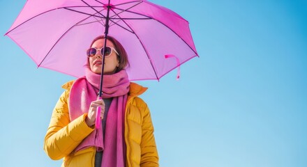 A stylish individual in a bold yellow puffer jacket and pink scarf confidently holds a translucent pink umbrella against a bright sky, embodying a joyful and carefree spirit.

