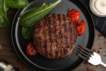 Naklejka premium Delicious grilled meat patty, tomatoes and spinach on wooden table, flat lay