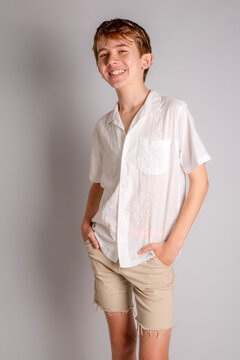 Studio portrait of a handsome smiling teenage boy posing in a white button up shirt and vintage khaki cut-off shorts