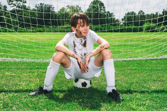 Youth soccer player sitting on a ball in the goal covered with mud