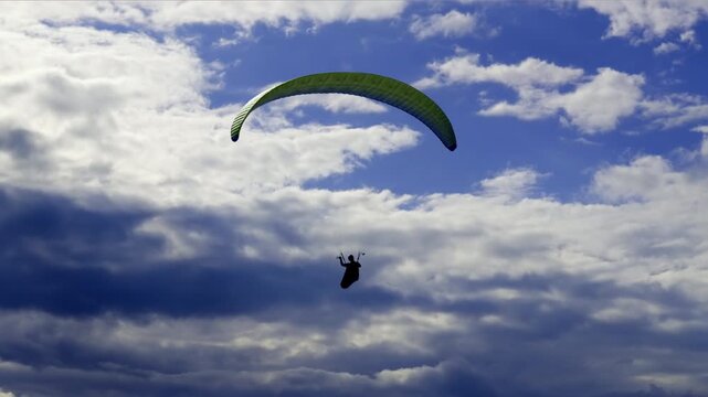 Silhouette of a paraglider flying high in the air, soaring gracefully through a dynamic blue sky filled with beautiful white and grey clouds, symbolizing freedom and adventure. South Sweden