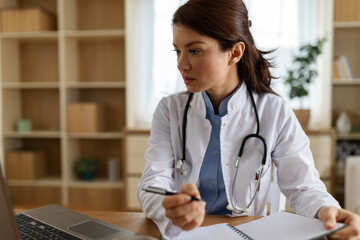 Doctor working at a desk with a laptop and notepad