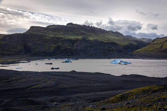 Solheimajokull glacier lagoon with floating blue icebergs and volcanic ash moraines, Iceland