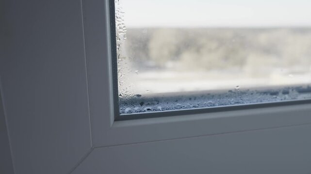 Close up view of water condensation droplets on a white plastic window frame corner inside a room. Concept of humidity, temperature difference, and household maintenance problems.