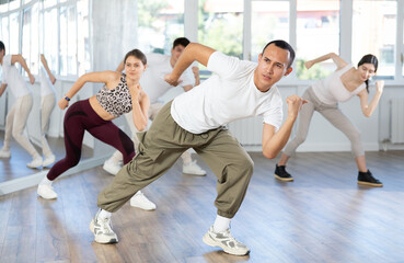 Fototapeta premium Enthusiastic smiling young Asian man in activewear energizing group during dance fitness class in well-lit mirrored studio
