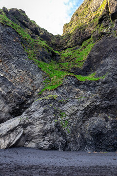 Bent basalt columns and mossy cliffs at Halsanefshellir Cave on Reynisfjara Black Sand Beach, Iceland