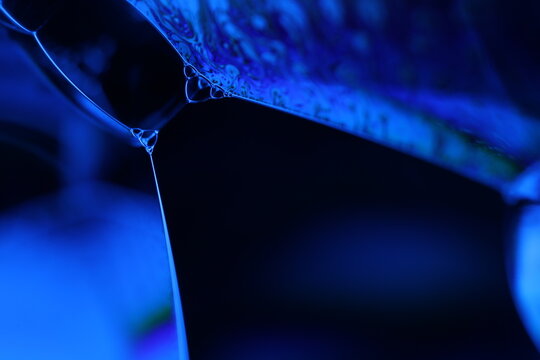 Abstract macro shot of blue liquid bubbles and a thin fluid thread. Artistic deep blue lighting creating a futuristic and scientific atmosphere. High-contrast texture with focus on surface tension
