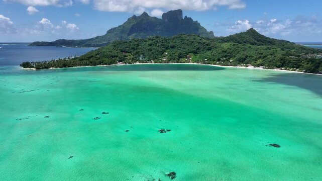 flying across turquoise South Pacific Ocean to Matira Beach, located on Bora Bora Island, French Polynesia with Mount Otemanu and Mount Pahia in the background - 4k aerial video footage