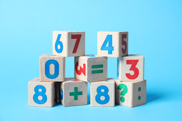 Wooden cubes with numbers and mathematical symbols on light blue background