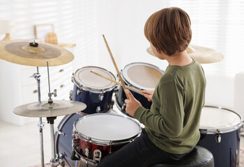 Obraz premium Little boy with drumsticks learning how to play drums indoors, back view