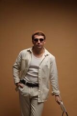 Fototapeta premium Fashion model. Handsome man in hat and sunglasses with chair against beige background