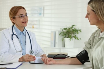 Smiling cardiologist in glasses measuring patient's blood pressure at table in hospital