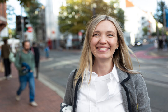 Portrait of young adult smiling happy confident cheerful blond woman walking on city street outdoors cityscape background. Female candid person headshot view joyful smile positive expression outside
