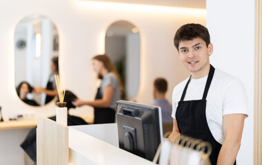 Young guy hairdresser stylist stands at cash register in beauty salon © JackF