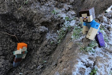Naklejka premium Minecraft action figure of smiling Steve spotted main female character figure of Alex on bottom of deep dug out garden pit. Winter half frozen garden soil around. 