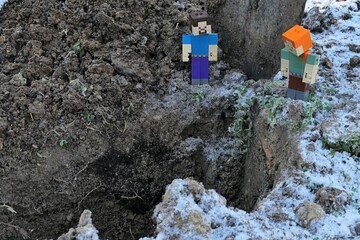 Naklejka premium Minecraft action figures of Steve and Alex standing on the corner of deep garden pit, frozen soil and some snow visible around. 