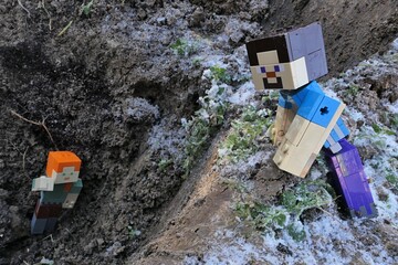 Naklejka premium Minecraft action figure of Steve watching main female characters Alex fallen into dug garden hole, traces of winter snow and frozen soil around. 