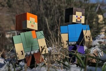 Naklejka premium Minecraft figures of Steve and Alex walking among stems of grass of garden lawn, partially covered with first winter snow, sunlit by afternoon sunshine. 