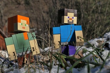 Naklejka premium Minecraft figures of Steve and Alex on a walk among stems of grass of garden lawn, partially covered with first winter snow, sunlit by afternoon sunshine. 
