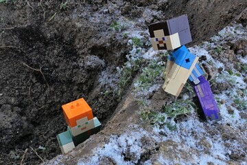 Naklejka premium Minecraft figure of main character Steve looking at her female friend Alex trying to get out from a pit in frozen winter garden, slightly covered with first snow. 