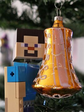 Minecraft actio figure of smiling main character Steve adoring golden coloured vintage bell shaped christmas tree decoration produced in socialistic Czechoslovakia during 1980s. 
