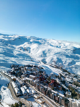 Drone panorama of Sierra Nevada ski resort in Spain, showing snowy mountains, alpine village buildings and clear blue sky, ideal for winter travel, tourism and holiday concepts.