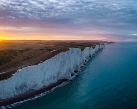 Aerial view of the chalk cliffs meeting the turquoise sea under a sky ablaze with dawn's first light, Seaford, England, United Kingdom.