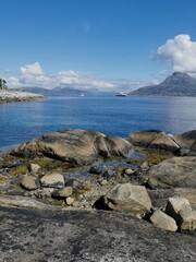 green meadow with houses on a fjord coast and mountains with clouds in the distance, norway