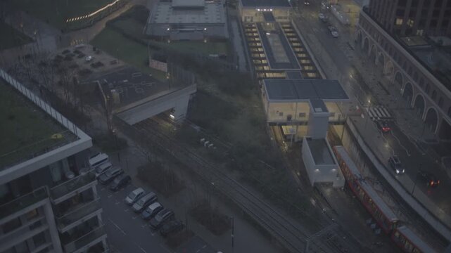 LONDON, UNITED KINGDOM &ndash; FEBRUARY 3, 2026: Elevated view of a DLR train traveling through Stratford beside modern buildings and wet streets at dusk.