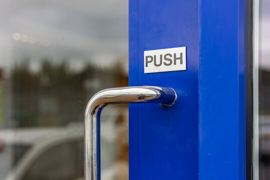 Close-up of metal door handle with push sign on blue frame and glass door