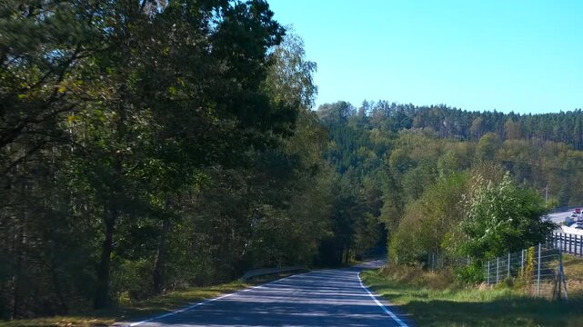 Car driving on country road through forest. Montage featuring six shots of a car driving along a country road surrounded by a lush forest. Sunlight filters through vibrant green trees