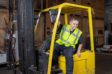 Warehouse worker climbing out of forklift truck wearing high-visibility vest © Tosh Lubek