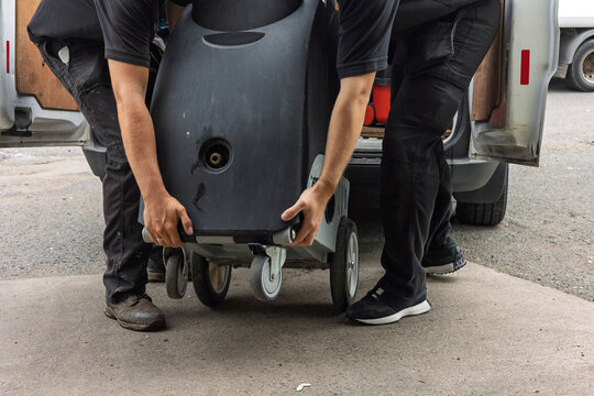 Workers placing industrial cleaning machine on ground behind service van