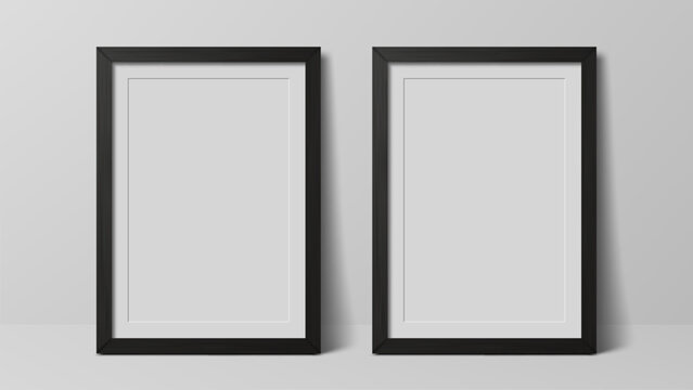 Two empty vertical photo frames in black stand on white wall. Realistic graphic design element for mockup template or product display.