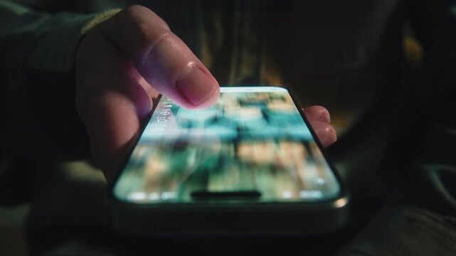 Extreme close-up male finger scrolling smartphone screen in deep darkness at night. Swiping finger, motion blur on phone screen. Evening online browsing, digital content consumption