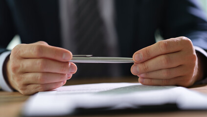 In a bright office, hands grip a pen thoughtfully above paperwork, reflecting a moment of concentration during a significant business meeting, emphasizing the importance of decisions being made.