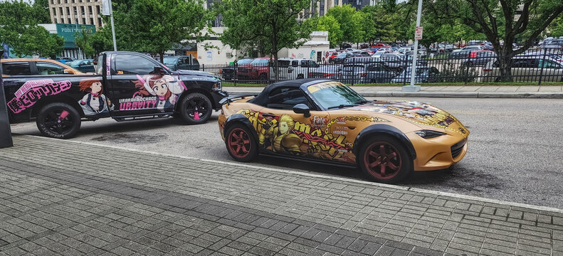 Two cars in a city with anime art on them (USA, July, 2024)