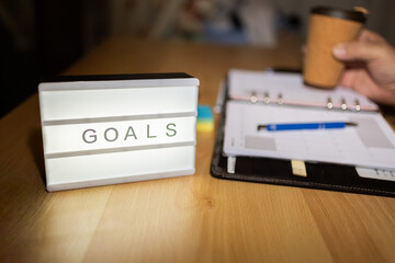 Goals lightbox on desk with planner and coffee