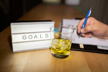 Hand writing goals with drink on wooden desk