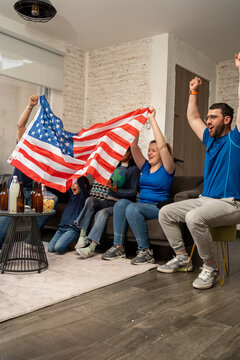 Family and friends cheering and celebrating football soccer at home with a USA flag, smiling together during an exciting match moment. Sports pride, friendship, shared joy, casual home viewing