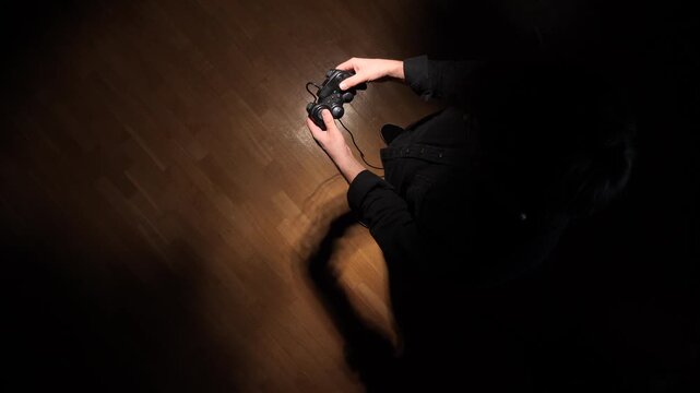 Person playing video games in a dimly lit setting, symbolizing loneliness, isolation, depression, or addiction to gaming, with only hands illuminated on the controller