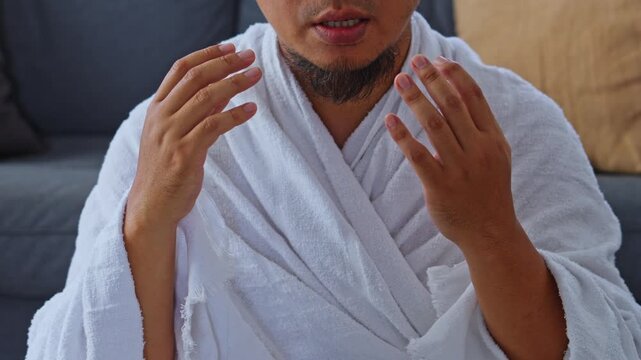 Muslim pilgrim in white Ihram clothing raising hands in sincere prayer and supplication