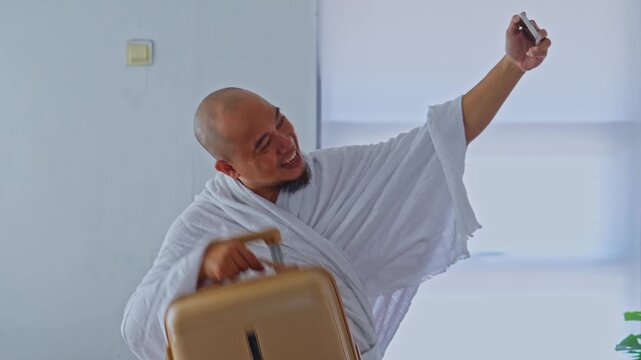 Happy pilgrim in Ihram cloth greeting gesture at smartphone camera before Hajj or Umroh